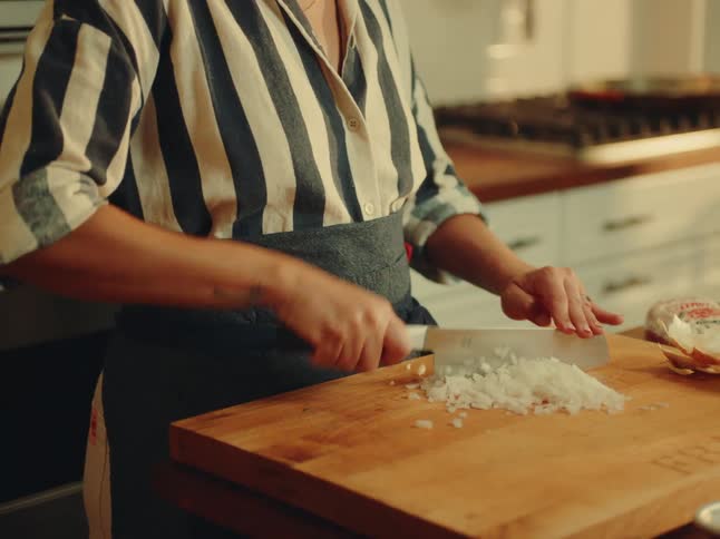 The woman is chopping onions n the kitchen