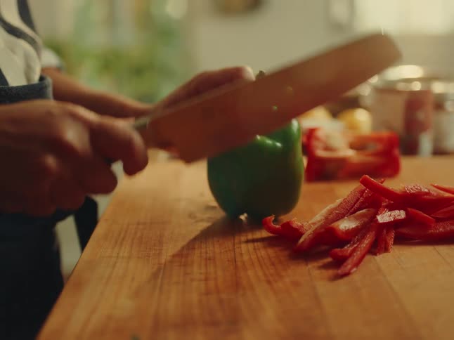 Woman with a knife cutting red bell peppers on a wooden cutting board