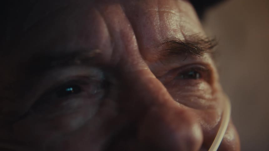 A very closeup shot focuses on the expressive wrinkled eyes of an elderly man subtly revealing an oxygen tube near his nostril as his gaze shifts slightly