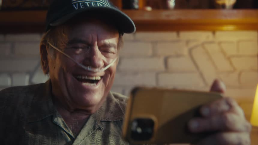 Elderly man in a cap laughing while watching on a smartphone