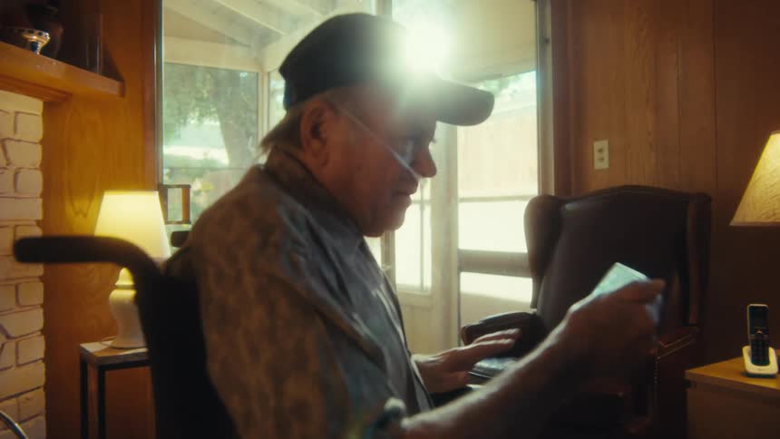 Elderly man sitting in wheelchair holding a smartphone and making a trembling expression