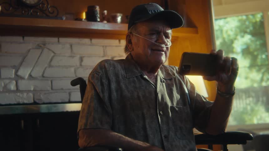 Elderly man in a wheelchair sitting in the living room interacting with a smartphone