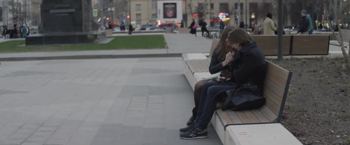 A man blows on a woman's hands while they sit on a bench