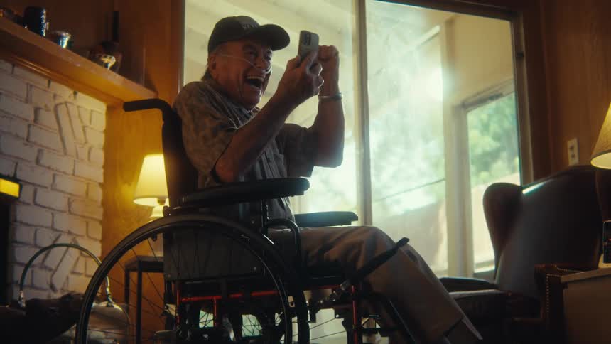 Elderly man in wheelchair celebrating and vibrating happily while watching on smartphone