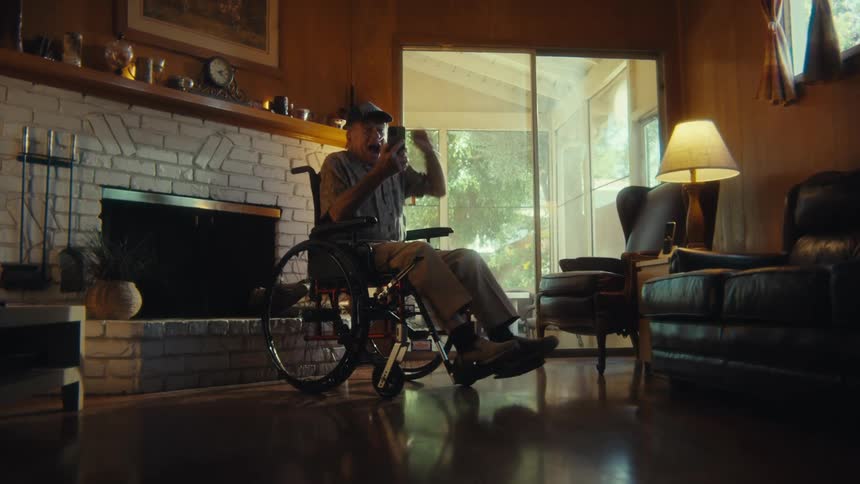 An old man in a wheelchair is excited by something on his phone