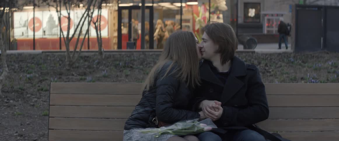 A man and woman sit together on a bench and kiss