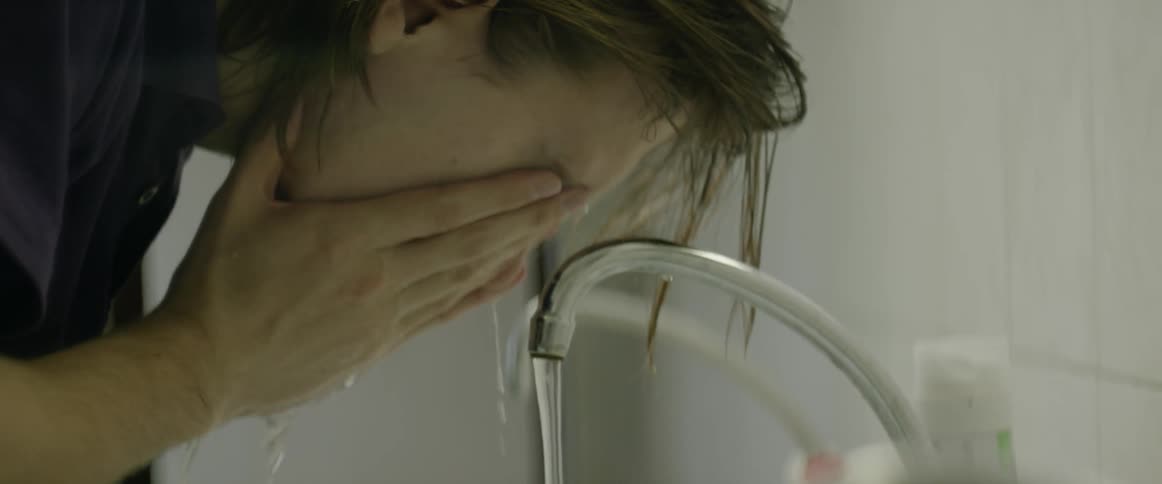A man standing at a sink filling his hands with water and washing his face