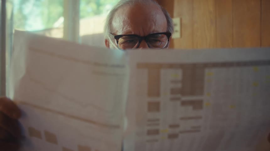 The man is reading a newspaper at home