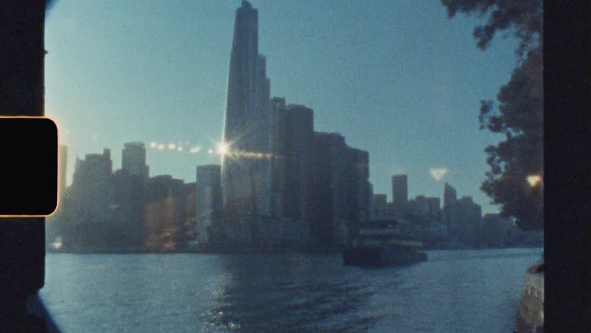 A boat cruising on the water with a city skyline along the coastline in the background at sunset