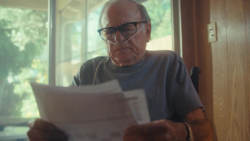 Elderly man sitting looking at documents and then taking out a smartphone