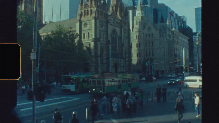 Pedestrians on the streets of a busy city with buildings and a church in the background