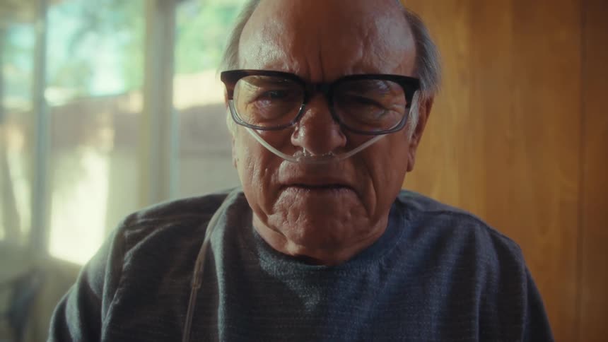 Elderly man with glasses sitting indoors looking at documents