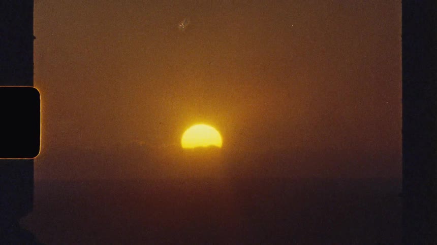 An orange sun sets on a cloudy evening casting a warm glow across the sky