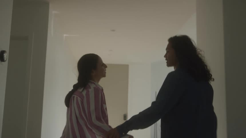 Two people are walking down a hallway holding hands they stop and turn to face each other talking with their hands appearing to be in a heated discussion