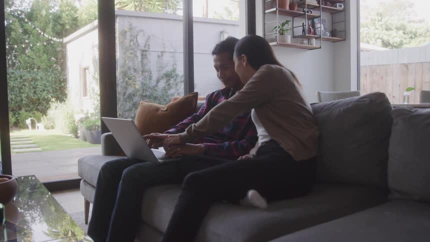 Woman and a man sitting on the living room sofa together interacting with a laptop