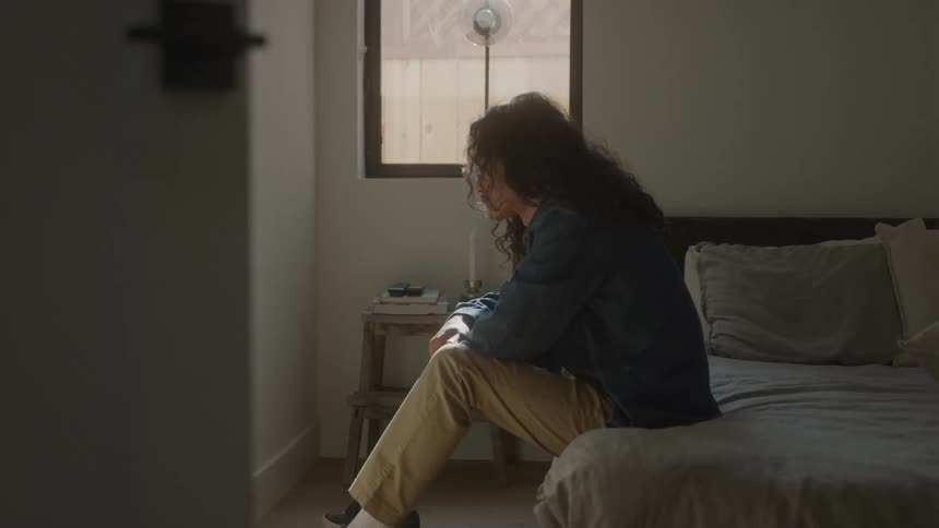 Curlyhaired man sitting on the bed with his head down