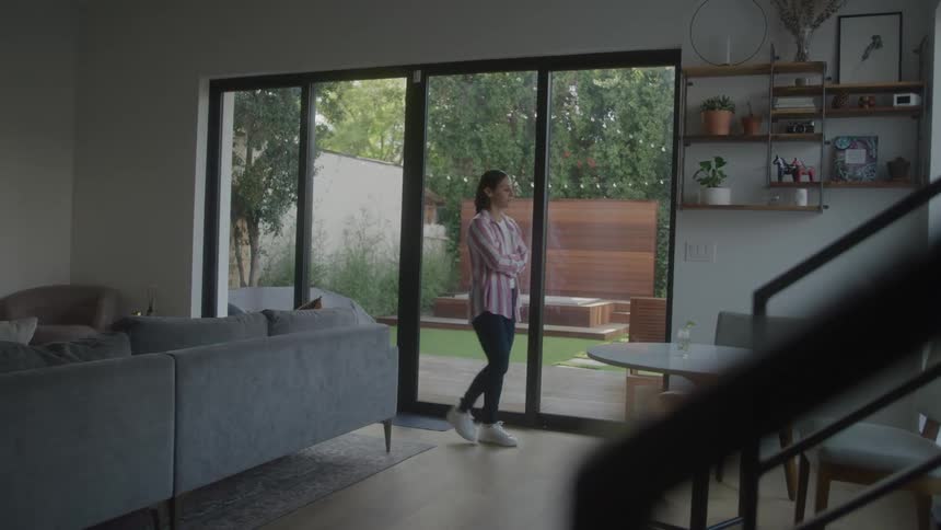 A young woman paces back and forth in her living room at midday looking worried and deep in thought