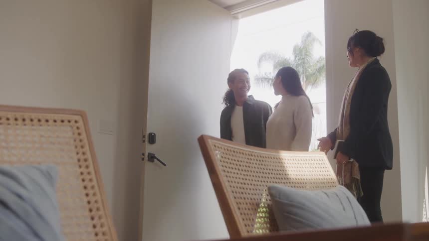 A couple walks into a home for inspection accompanied by a building agent all smiling warmly as they enter