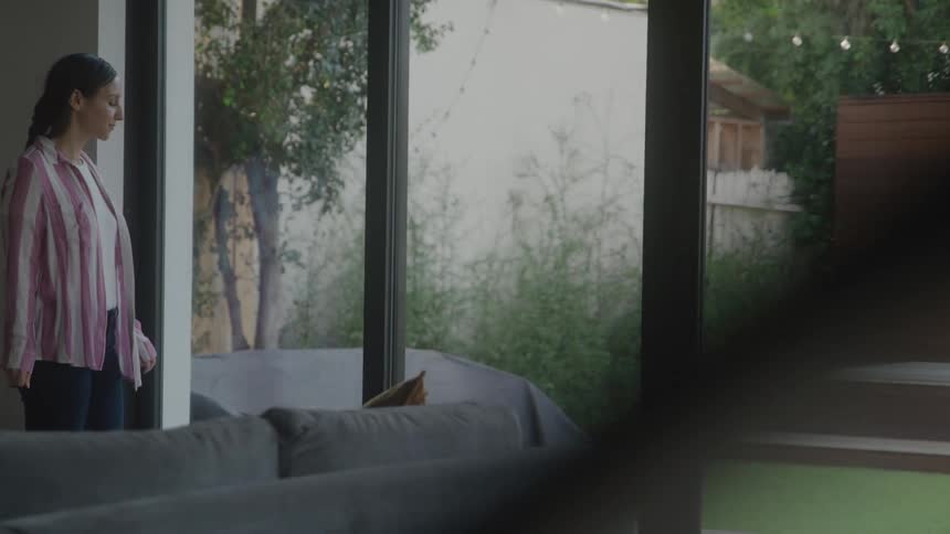 Woman paces distractedly in a modern living room near large glass windows