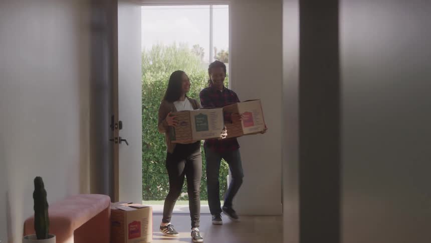 Couple enters home together carrying a package box