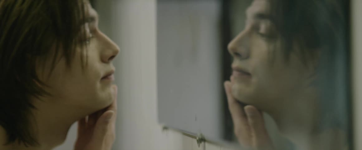 A young man rubs his face while looking in a mirror