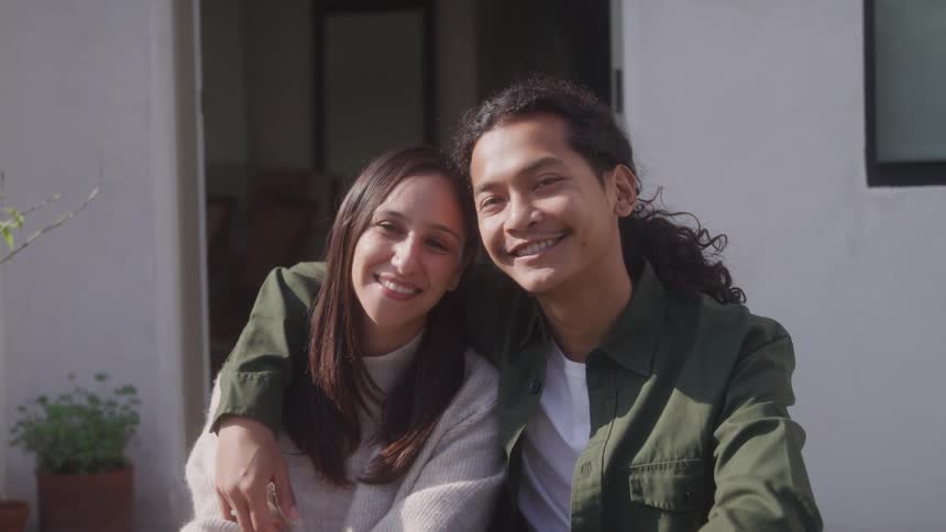 A portrait of a man and a woman who are smiling and sitting in front of a house and hugging each other