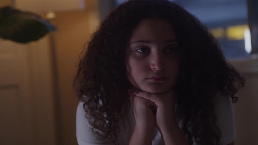 Young girl sits quietly appearing upset and deep in thought