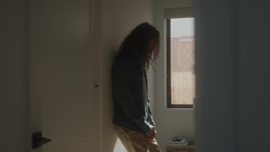 Curlyhaired man with his head down leaning against the wall of a room in the house