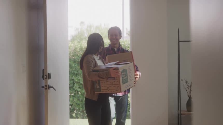 Couple moves in carrying boxes into their new home