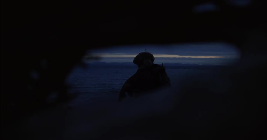 The video shows a dark silhouette of a person from behind wearing a hat and possibly carrying a backpack looking towards a dimly lit horizon over what appears to be a vast flat landscape the scene is viewed through a dark irregularly shaped opening
