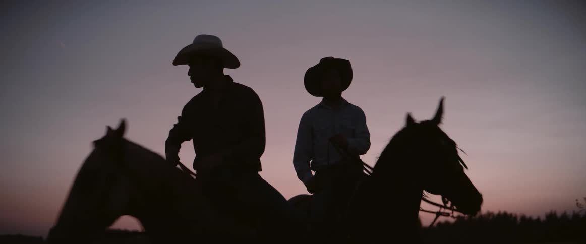 Pair of rancher silhouettes horseback riding in the countryside at dusk