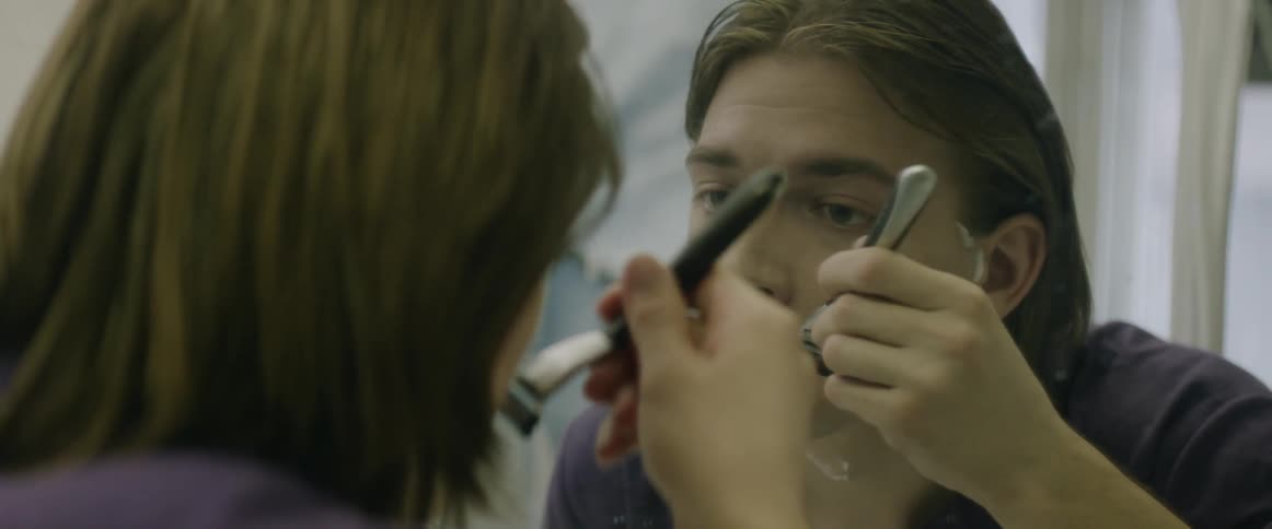 A man is shaving his face in the mirror