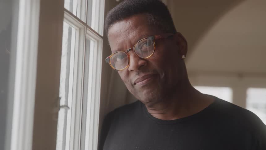 The man smiles while leaning against the window