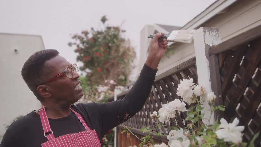 Man uses a small paintbrush to paint a fence post white