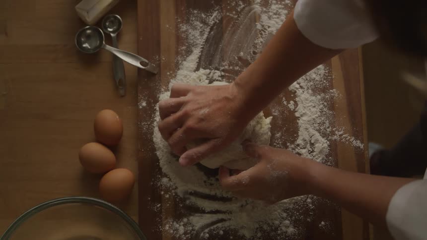A person molds dough while sprinkling flour to smooth it with three eggs placed on the side