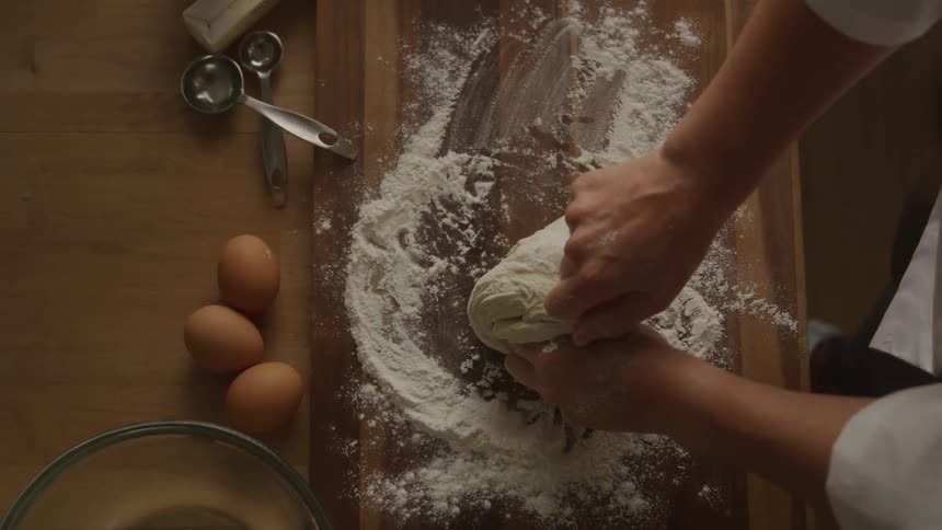 Overhead view baker kneading dough on floured wood cutting board