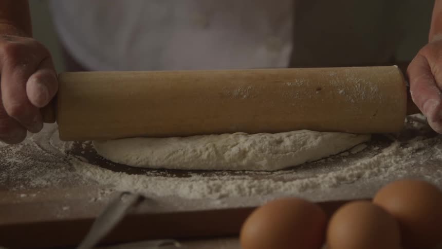 Woman uses a wood rolling pin to rollout a circle of dough