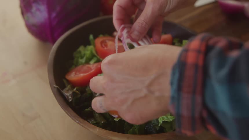 A person preparing sliced vegetables in a bowl by adding sliced onions to it