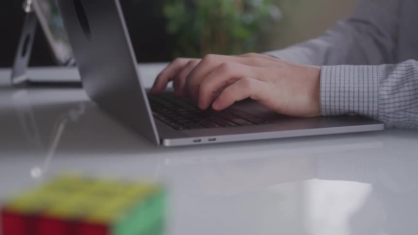 A closeup shot of a mans hands typing on a laptop keyboard on a white desk with a blurred background