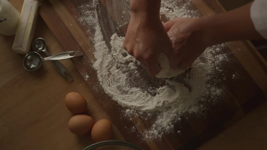 Overhead view baker kneading dough on floured wood cutting board