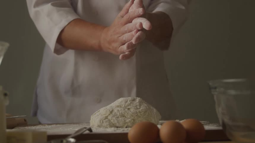 Chef clapping his hands with wheat flour on top of a dough