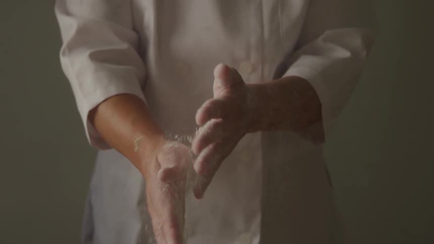 A chef rubs flour on her arms rubbing them together as the flour falls off