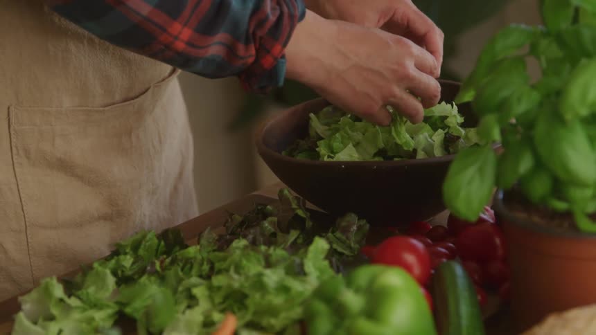 A woman picks up sliced vegetables and places them in a bowl on a table filled with other produce