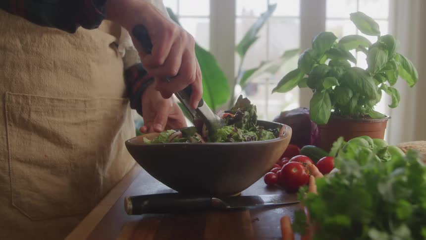 Person tossing a green leafy salad in a wood salad bowl