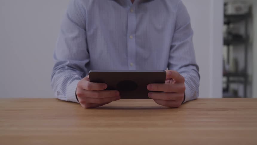 A person watches content on a tablet while sitting in front of a table