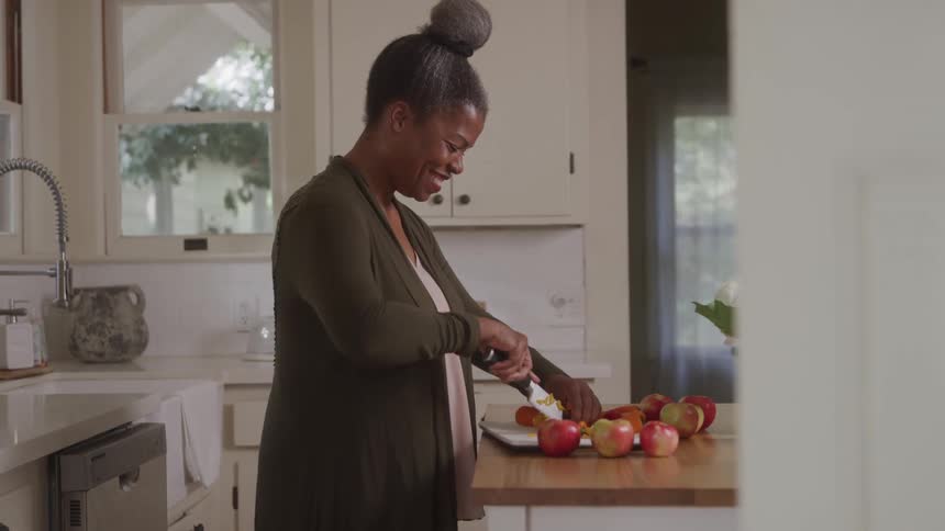 Cheery woman cutting apples on counter in her kitchen