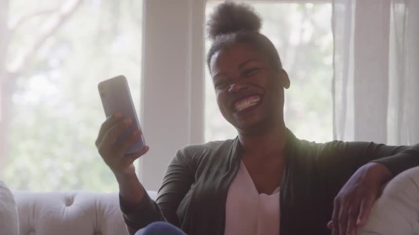 Woman sitting on the couch laughing while looking at her smartphone