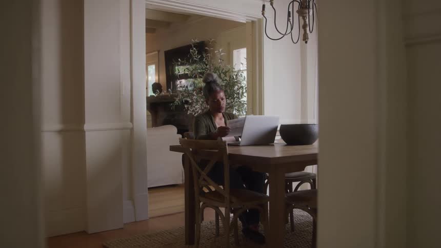 The woman uses her laptop on the dining room