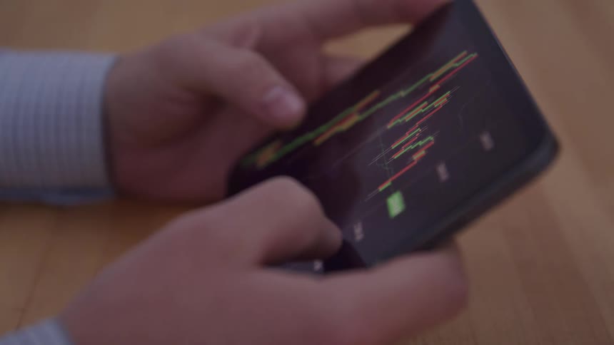 A closeup shot of a persons hands holding a smartphone actively scrolling and analyzing a financial trading chart displayed on the screen