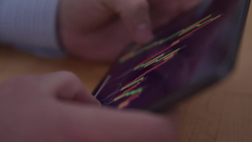 A persons hands are shown holding a tablet displaying colorful graphs or charts with their fingers interacting with the screen the background is blurred suggesting an indoor setting